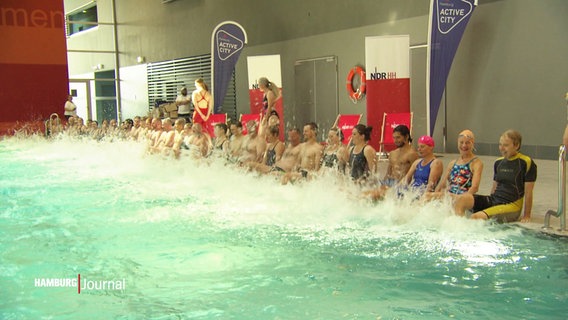 Glücklich ausgebildete Schwimmlehrer:innen sitzen am Beckenrand und planschen mit den Füßen. © Screenshot 