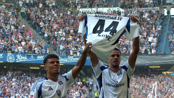 Zwei Spieler des HSV halten ein Tricot mit der Nummer 44. © Screenshot 