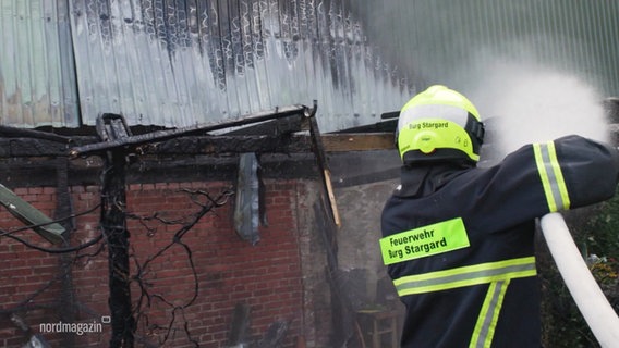 Ein Feuerwehrmann löscht mit Wasser aus einem Schlauch einen Hausbrand. © Screenshot 