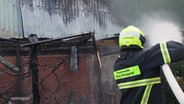 Ein Feuerwehrmann löscht mit Wasser aus einem Schlauch einen Hausbrand. © Screenshot 