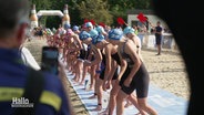 An einer Startlinie an einem Strand stehen viele Triathleten vor dem Startschuss. © Screenshot 