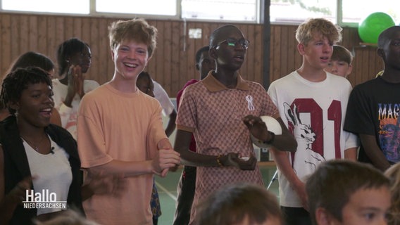 In einer Schule stehen deutsche Schülerinnen und Schüler mit ihren senegalesischen Austauschpartnerinnen und -partnern zusammen. © Screenshot 