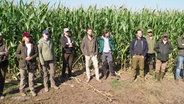 Eine Gruppe von Jagdschein-Anwärterinnen und -Anwärtern steht auf einer Lichtung in einem Maisfeld. © Screenshot 