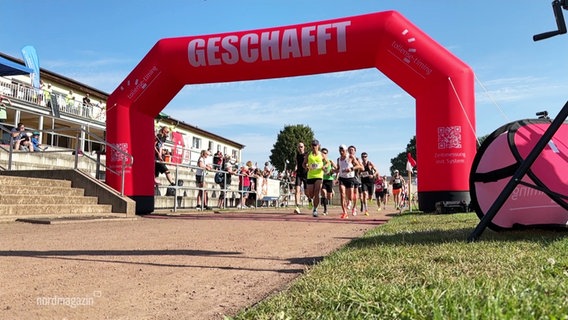 Blick auf den Zieleinlauf unter einem roten Torbogen bei einem Marathon © Screenshot 