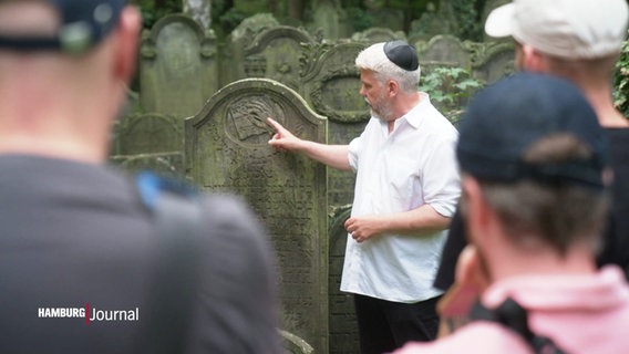 Ein Mann mit Kippa erklärt einen Grabstein auf dem Jüdischen Friedhof Altona. © Screenshot 