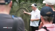 Ein Mann mit Kippa erklärt einen Grabstein auf dem Jüdischen Friedhof Altona. © Screenshot 