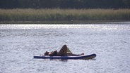 Eine Person sonnt sich auf einem Boot im Wasser. © Screenshot 