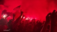 Singende Fans mit erhobenen Händen, rotes Licht und Nebel bei einem Konzert. © Screenshot 