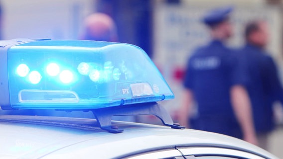 Ein Blaulicht eines Polizeiwagens in Nahaufnahme, im Hintergrund unscharf Polizeibeamte. © Screenshot 