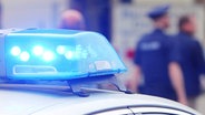 Ein Blaulicht eines Polizeiwagens in Nahaufnahme, im Hintergrund unscharf Polizeibeamte. © Screenshot 