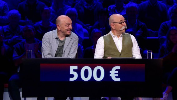 Im Studio von "Wer weiß denn sowas?" sitzen Bernhard Hoëcker und Horst Lichter gemeinsam an einem Pult. © Screenshot 