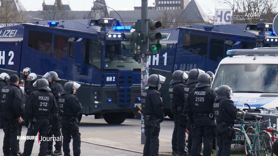 Bild eines Polizeiaufgebotes mit Einsatzkräften in schwarzen Overalls, mit Helmen und bewaffnet sowie Wasserwerfern. © Screenshot 