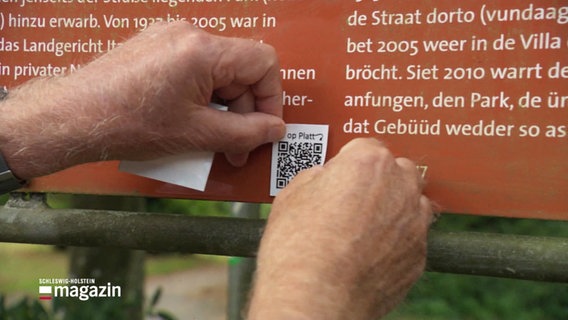 Ein Sticker mit einem QR-Code wird auf eine Texttafel geklebt. © Screenshot 