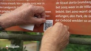 Ein Sticker mit einem QR-Code wird auf eine Texttafel geklebt. © Screenshot 