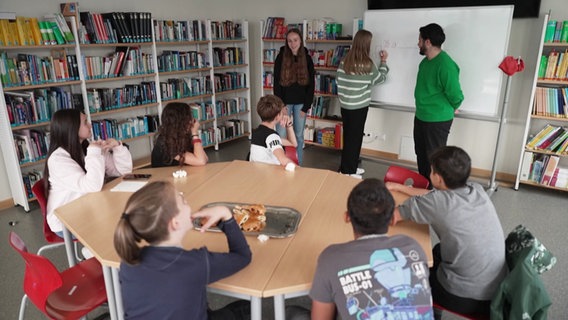 Schülerinnen und Schüler sitzen an einem Tisch. © Screenshot 