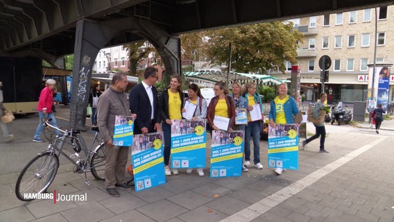 Eine Erwachsenen-Gruppe posiert mit Plakaten unter der Isebrücke in Hamburg. © Screenshot 