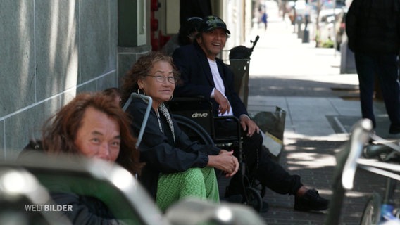 Menschen sitzen an einer Straße. © Screenshot 