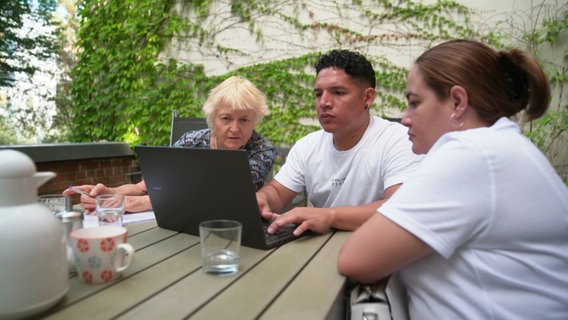 Das Ehepaar Real-Corea aus Nicaragua sitzt mit Wohnungslotsin Ulrike Hanemann vor einem Laptop und sichtet Wohnungsanzeigen. © Screenshot 