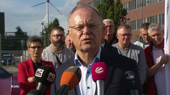 Stephan Weil steht in Emden vor dem VW-Werk. Im Hintergrund Beschäftigte. © Screenshot 