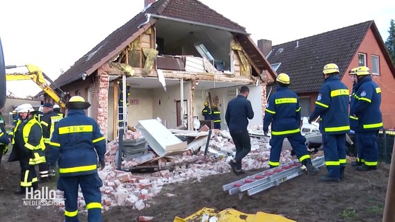 THW-Einsatzkräfte stehen vor einem Haus, dessen komplette Giebelwand eingestürzt ist. © Screenshot 