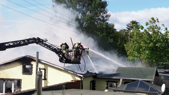 Zwei Feuerwehrleute löschen per Drehleiter den Dachstuhl eines Hauses. © Screenshot 