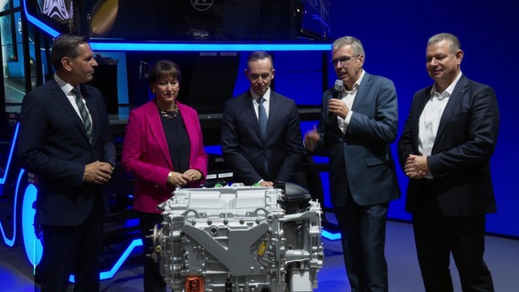 Vier Männer und eine Frau stehen vor einem ausgestellten Wasserstoffmotor. © Screenshot 