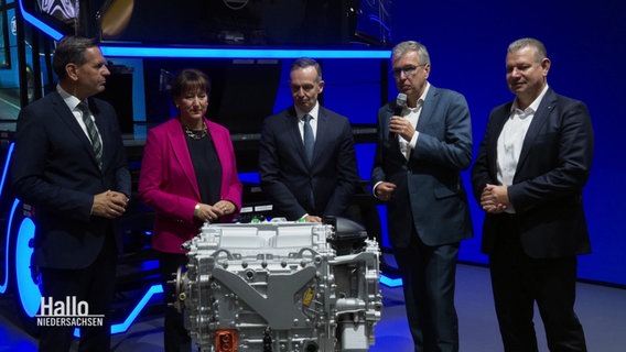 Hildegard Müller vom Verband der Automobilindustrie steht mit vier weiteren Messe-Gästen vor einem ausgestellten Wasserstoffmotor. © Screenshot 