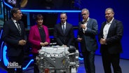 Hildegard Müller vom Verband der Automobilindustrie steht mit vier weiteren Messe-Gästen vor einem ausgestellten Wasserstoffmotor. © Screenshot 