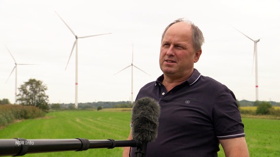 Ein Mann vor mehreren Windrädern spricht in ein Mikrofon. © Screenshot 