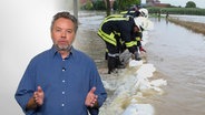 Journalist Eckhardt Reimann gestikuliert. Hinter ihm ist ein Bild eingeblendet, auf dem Feuerwehrleute ein Hochwasser mit Sandsäcken eindämmen. © Screenshot 