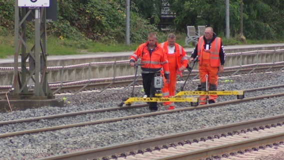 Gleisarbeiter der Deutschen Bahn in oranger Arbeitskleidung und mit Arbeitsgerät auf den Schienen. © Screenshot 