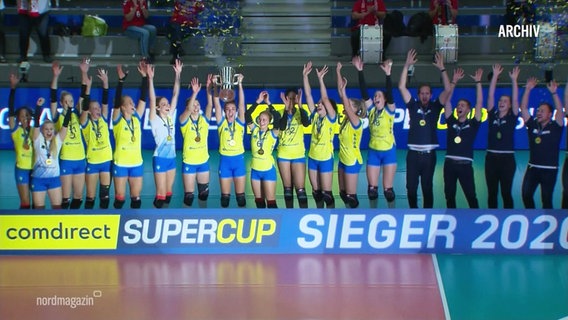 Bild bei der Siegerehrung des Supercup 2020: Der SSC Palmberg Schwerin auf dem Podium, die Arme jubelnd in die Luft gestreckt. (Archivbild) © Screenshot 