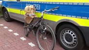 Ein kaputtes Fahrrad lehnt an einem Polizeifahrzeug. © Screenshot 