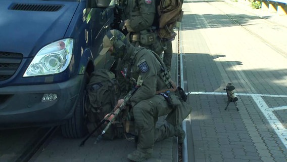 Ein Polizist in Tarnkleidung sucht hinter einem Auto Schutz. © Screenshot 