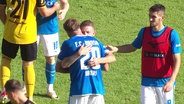 Zwei Spieler des FC Hansa Rostock umarmen sich auf einem Spielfeld. © Screenshot 