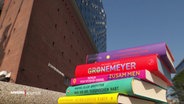 Ein Stapel Bücher liegt auf dem Boden vor der Elbphilharmonie. © Screenshot 