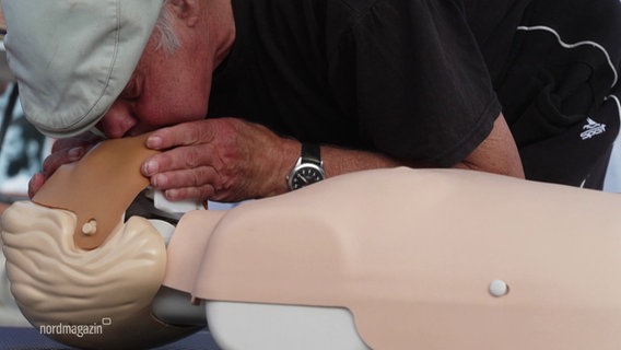 Ein älterer Herr führt eine Mundzumundbeatmung bei einem Dummy durch, um den Weltrekord für die längste Reanimation nach Boizenburg zu holen. © Screenshot 