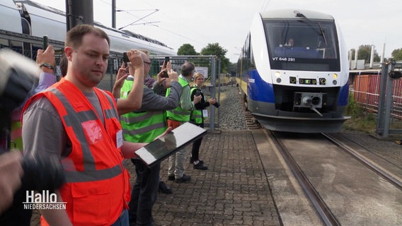 Menschen in grünen Warnwesten schauen einem Zug beim Einfahren zu. © Screenshot 