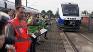 Menschen in grünen Warnwesten schauen einem Zug beim Einfahren zu. © Screenshot 