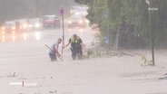 Ein Polizist und ein weiterer Mann versuchen eine überflutete Straße von Debris freizumachen. © Screenshot 