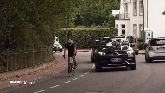 Ein Radfahrer auf einem Fahrradstreifen am Rande einer Straße wird von einem Auto überholt. © Screenshot 