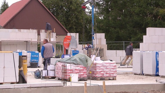 Auf einer Baustelle für ein Haus steht Baumaterial im Rohbau. © Screenshot 