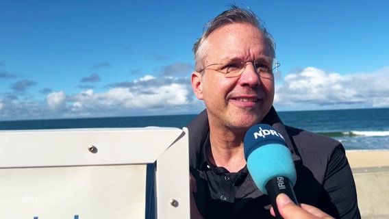 Sylts Bürgermeister Nikolas Häckel steht an einem Strandkorb und wird vom NDR interviewt. © Screenshot 