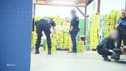 Polizeibeamte stellen in einer Lagerhalle viele mit Kokain beladene Bananenkisten sicher. © Screenshot 