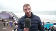 Reprter Patrick Halatsch steht in Westerland auf Sylt an der Strandpromenade und berichtet. © Screenshot 