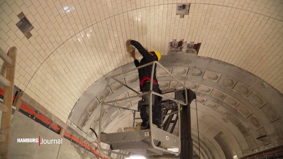 Ein Arbeiter bringt Fliesen an der gebogenen Decke des Alten Elbtunnels an. © Screenshot 