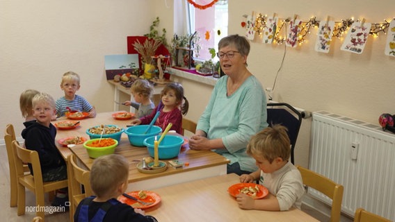 Eine Erzieherin sitzt mit sieben Kita-Kindern beim Essen am Tisch. © Screenshot 