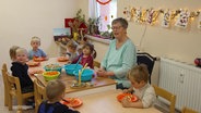 Eine Erzieherin sitzt mit sieben Kita-Kindern beim Essen am Tisch. © Screenshot 