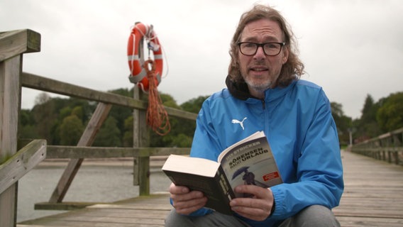 Autor Sven Stricker sitzt auf einer Brücke und liest aus seinem Buch der Sörensen-Reihe. © Screenshot 