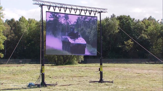 Eine Leinwand auf einer Wiese, auf der ein fahrendes Militärfahrzeug zu sehen ist. © Screenshot 